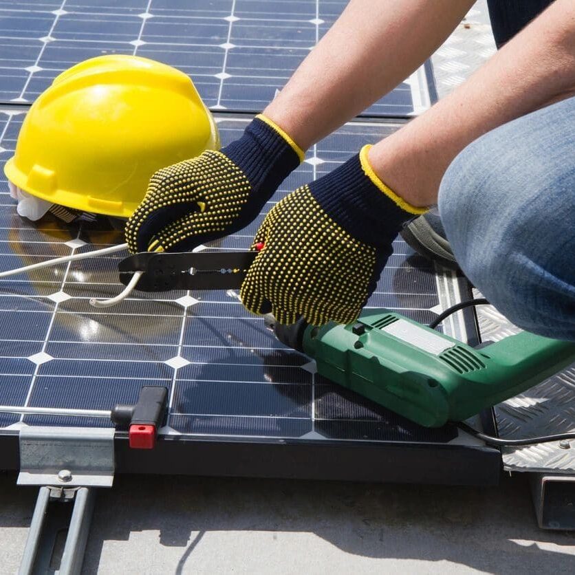 A person with gloves and hard hat working on solar panel.