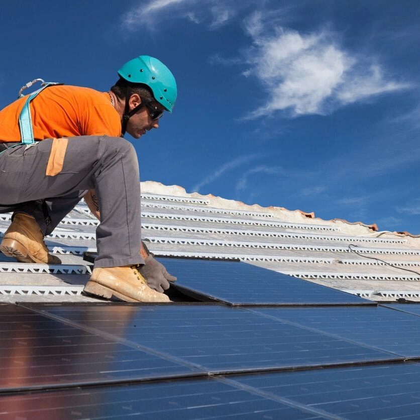 A man in an orange shirt and blue helmet is working on solar panels.